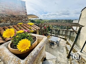 A rooftop terrace with potted yellow flowers, a table with chairs, and a view of the countryside. - Chez Mathilde - SAISSAC (SAISSAC)