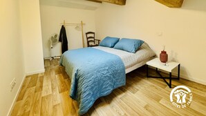 Un dormitorio con una cama, una silla, una mesita, un ventilador y una lámpara colgante.