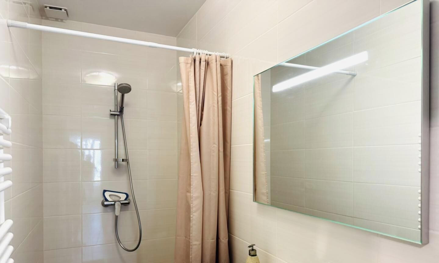 Et moderne badeværelse med en glasbrusekabine, en hvid vask med kromarmatur og et beige brusehængsel.