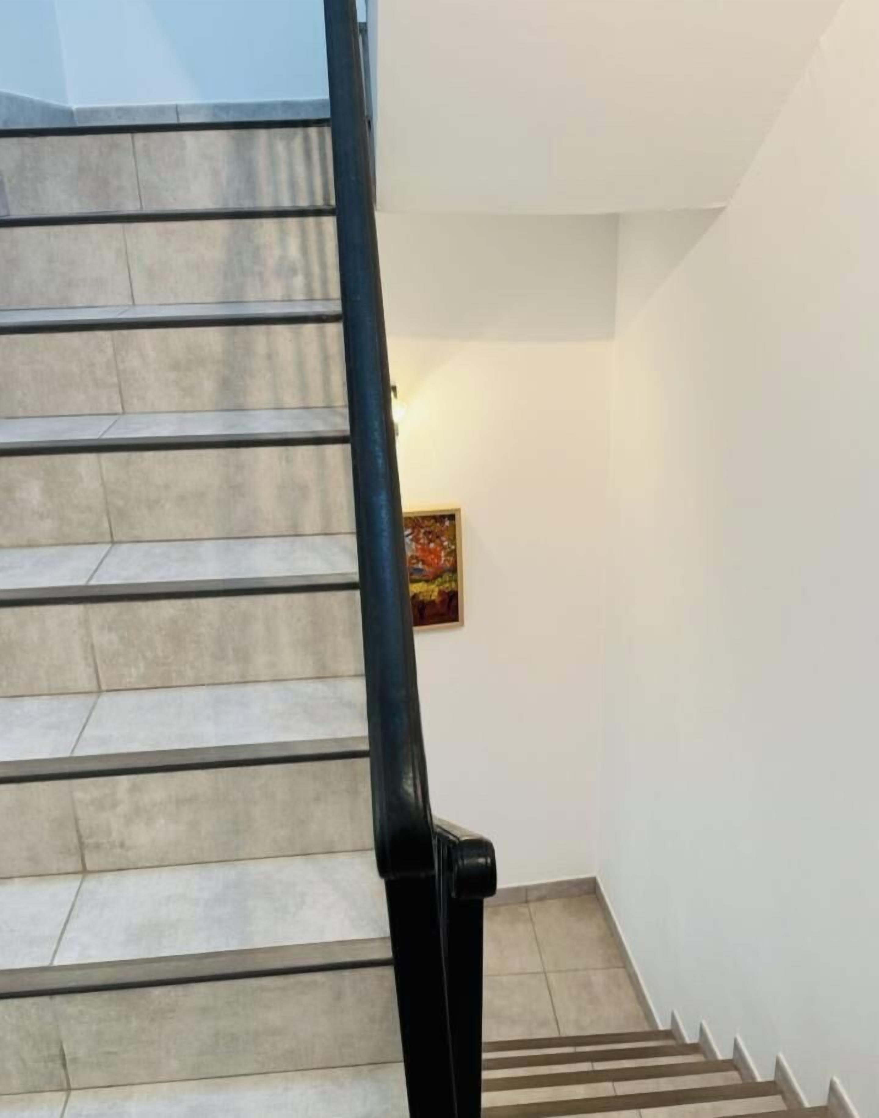 A staircase with beige tiles and black handrails, leading to a landing with a framed picture.