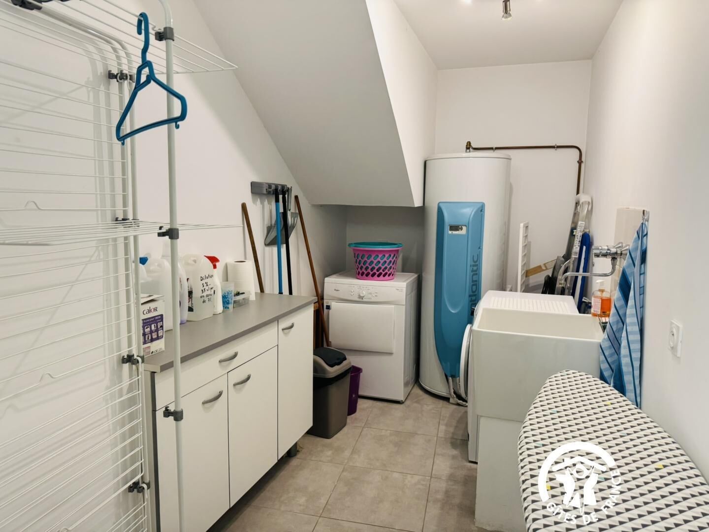 Une petite buanderie comprenant un lave-linge, un étendoir et une petite planche à repasser.