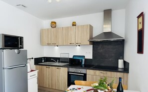 A modern kitchen with a microwave, oven, sink, and a dining area with a table set for two. - Lou Courredou - FERRALS LES CORBIERES (FERRALS LES CORBIERES)