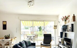 A living room with a sofa, armchair, dining table, and chairs. There is a TV stand with a TV and a bookshelf. A yellow umbrella is outside the sliding glass door. - Lou Courredou - FERRALS LES CORBIERES (FERRALS LES CORBIERES)