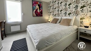 Un dormitorio con cama, mesita de noche, silla, ventana y pared con diseño de hojas.