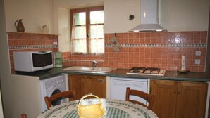 A compact kitchen with a sink, stove, microwave, and dishwasher. There is a table with a checkered tablecloth and chairs. - Domaine du Coude - SAINT ANDRE DE ROQUELONGUE (SAINT ANDRE DE ROQUELONGUE)