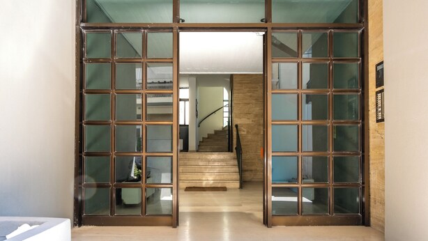 A modern interior with a staircase leading to an upper floor, a glass door entrance, and a clean, tiled floor. - Cozy Central Apartment by HOM54 (Heraklion)