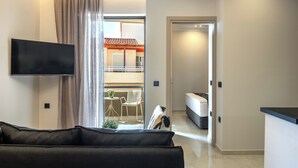 A modern living room with a flat-screen TV, a sofa, and a view of a balcony with a dining area. - Cozy Central Apartment by HOM54 (Heraklion)