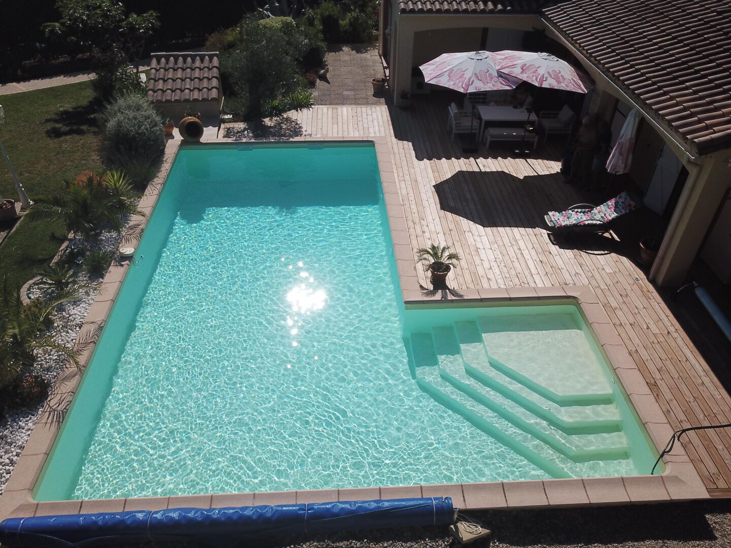 Una piscina rectangular con agua cristalina, rodeada por una terraza de madera y un porche cubierto con mobiliario exterior.
