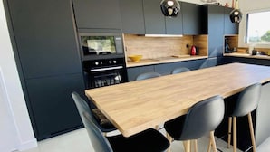 A modern kitchen with a central island, black chairs, and pendant lighting.