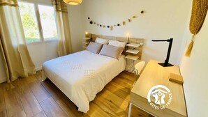 A bedroom with a bed, bedside tables, a desk, a hanging lamp, and a window with curtains.