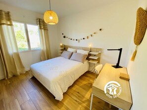 Une chambre à coucher comprenant un lit, des tables de chevet, un bureau, une lampe suspendue et une fenêtre avec des rideaux.