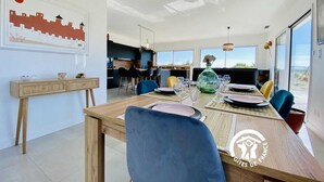 A modern dining area with a wooden table, blue chairs, and a view of the kitchen in the background.