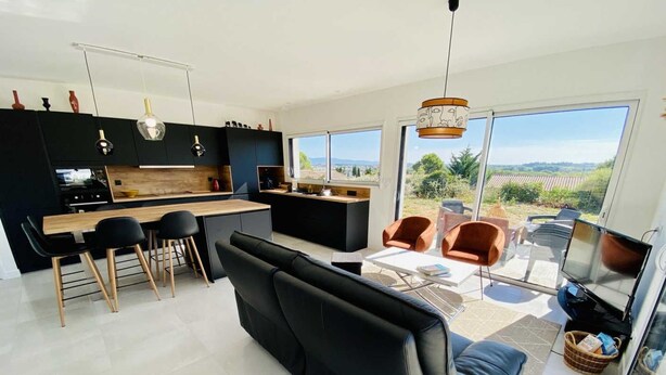 A modern kitchen with black cabinets, a wooden countertop, and a dining area with black chairs and a black sofa.