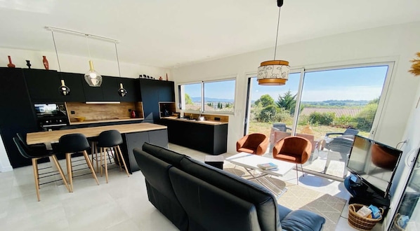 A modern kitchen with black cabinets, a wooden countertop, and a dining area with black chairs and a black sofa.