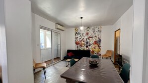 A dining area with a large table, chairs, a sofa, and a floral wall mural. - Chez Madou - ROQUEFORT DES CORBIERES (ROQUEFORT DES CORBIERES)
