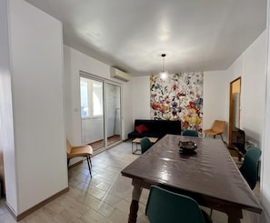 Ein Essbereich mit großem Tisch, Stühlen, einer Couch und einer Wandmalerei mit floralem Dekor.