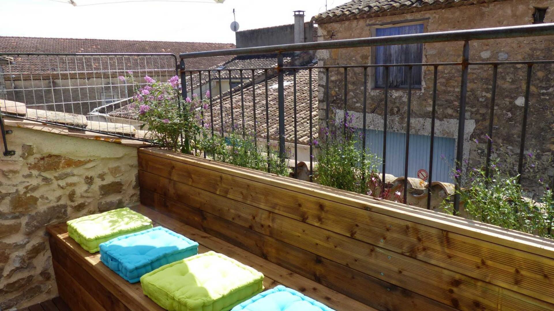 Un balcón con barandillas de madera, un muro de piedra y vistas a un edificio tradicional con tejas de terracota.