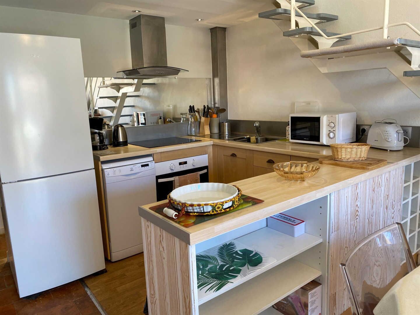 Une cuisine moderne équipée d’un réfrigérateur, d’un lave-vaisselle, d’un four à micro-ondes et d’un plan de travail en bois sur lequel se trouve un saladier.