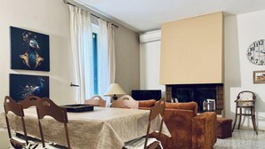 A room with a dining table, chairs, a sofa, a fireplace, and artwork on the walls.
