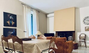A room with a dining table, chairs, a sofa, a fireplace, and artwork on the walls.