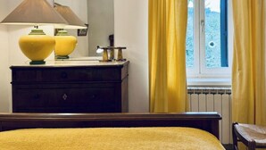 A bedroom with a bed, a dresser with a mirror, a lamp, and yellow curtains.