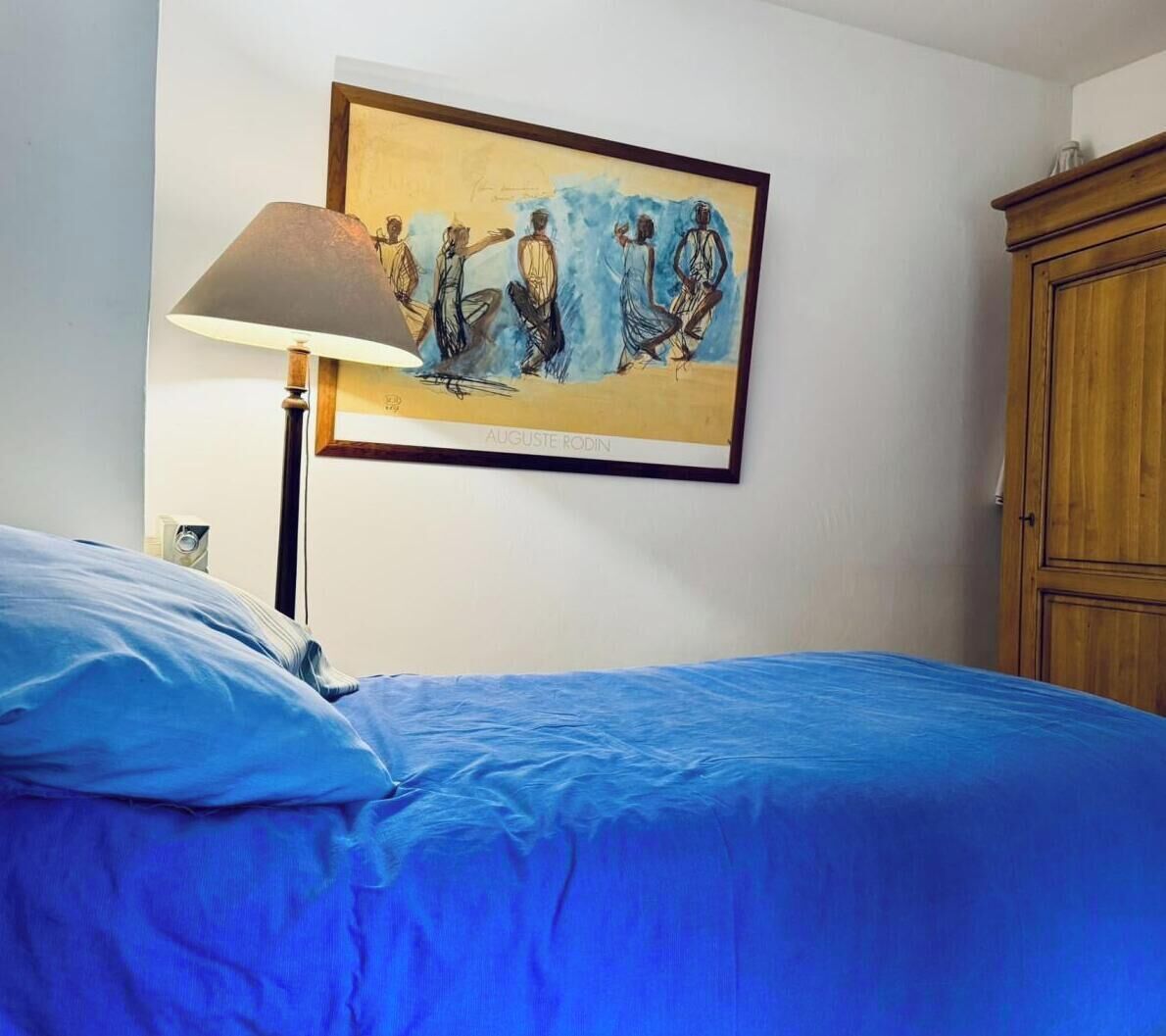 Une pièce comprenant un lit, une lampe, un tableau et une armoire en bois.