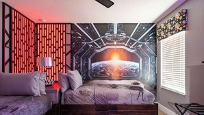 Een slaapkamer met een bed, een nachtkastje, een lamp en een muurschildering van een ruimte.