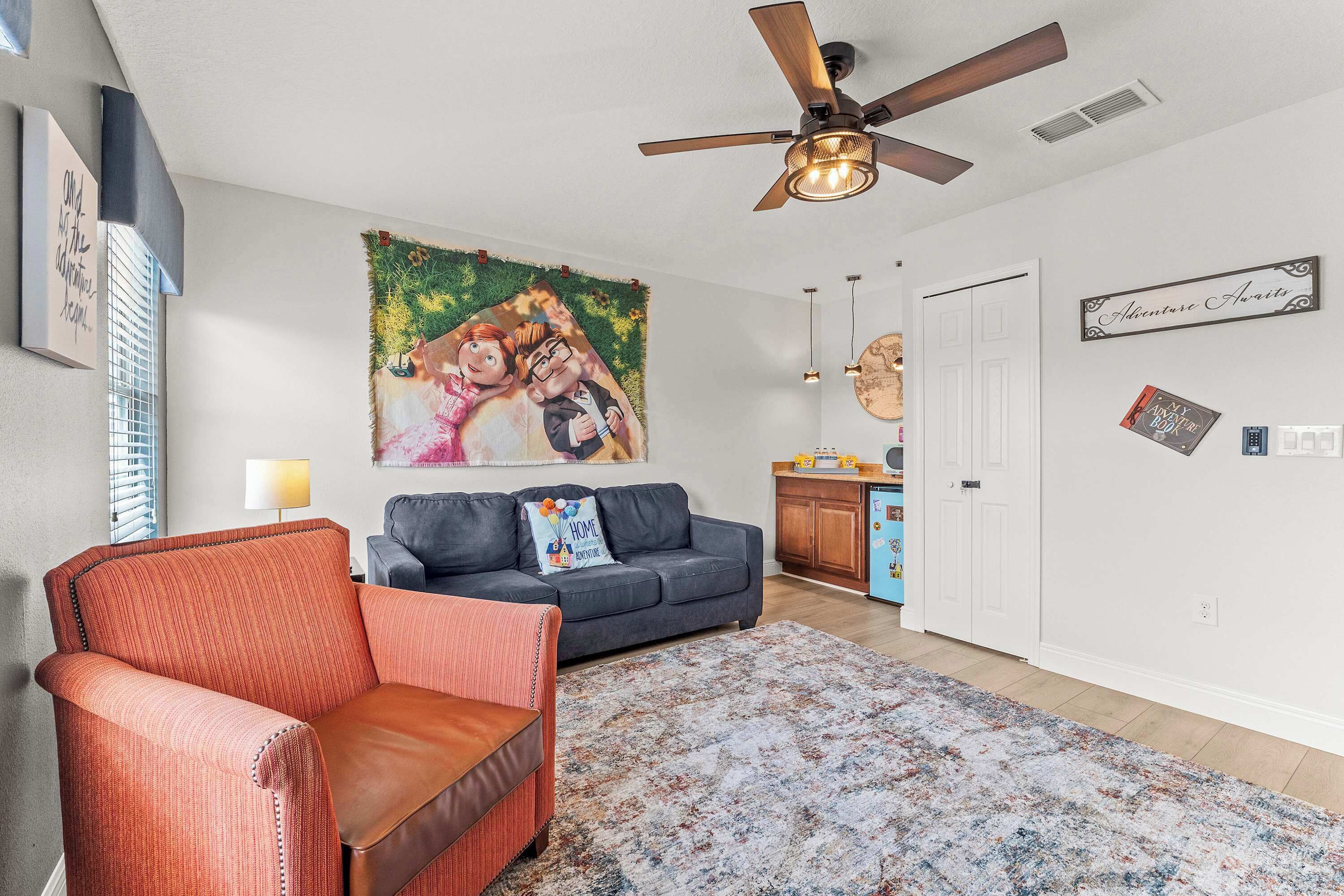 A living room with a ceiling fan, a sofa, a chair, a rug, and a painting on the wall.