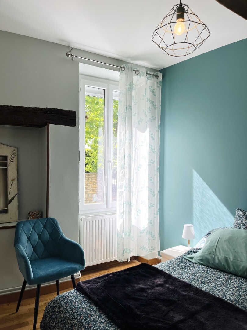 Een slaapkamer met een bed, een stoel, een raam met gordijnen en een hanglamp.