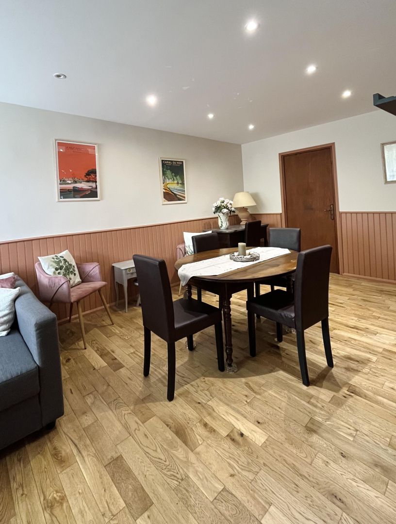 Un comedor con una mesa y sillas de madera, una mesita auxiliar con una lámpara y una puerta al fondo.