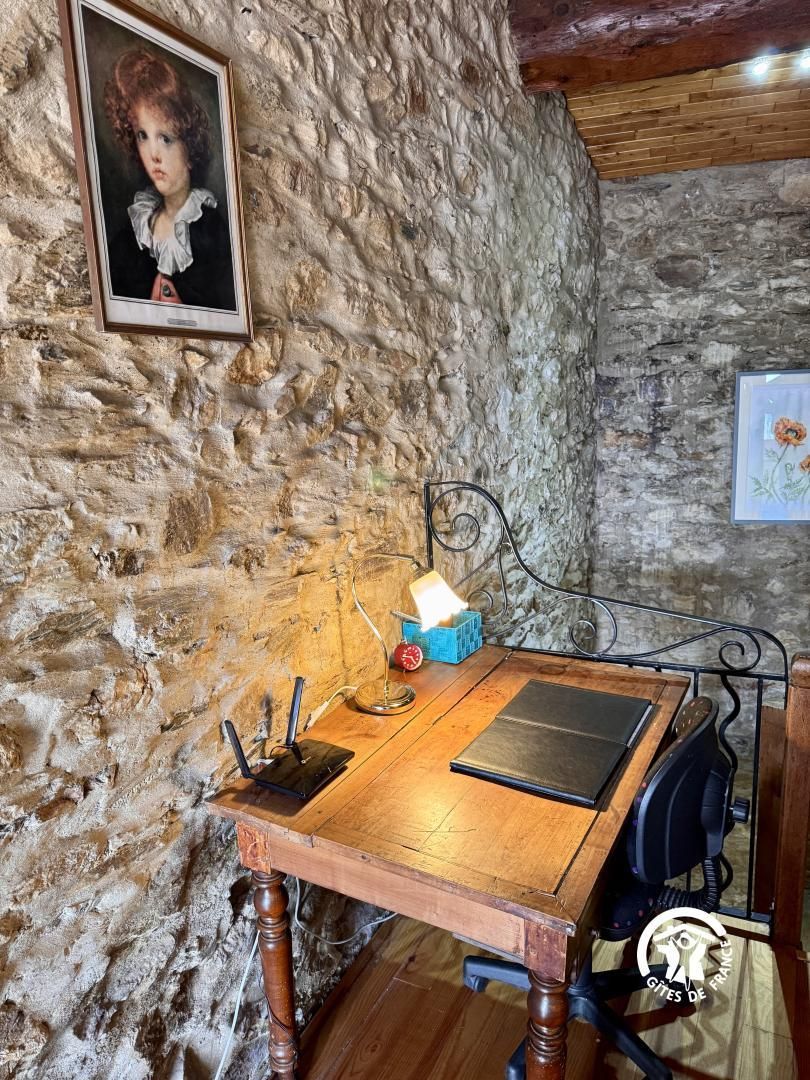 Una stanza rustica con una parete in pietra, un tavolo in legno con un portatile, una lampada e un quadro incorniciato.