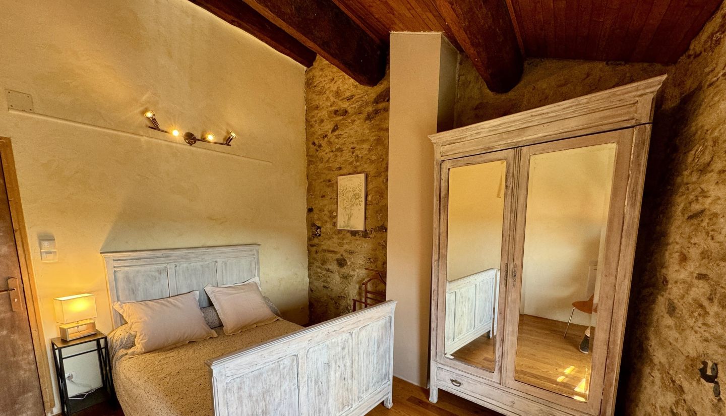 A bedroom with a wooden bed, a nightstand, a wardrobe, and a stone wall.