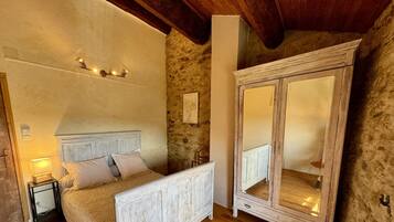 A bedroom with a wooden bed, a nightstand, a wardrobe, and a stone wall.