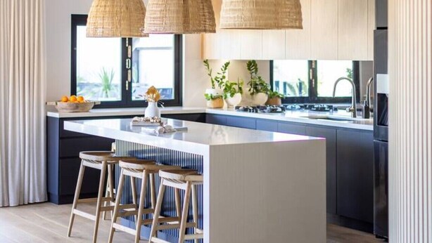 Een moderne keuken met een centraal eiland, hanglampen en uitzicht buiten.