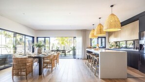 Een moderne keuken met een centraal eiland, een eetgedeelte met rieten meubels en grote ramen.