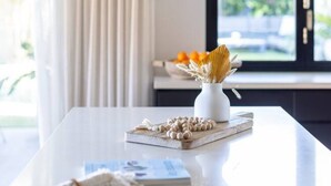 Een moderne eethoek met een witte tafel, een geweven hanglamp en uitzicht op de omgeving door grote ramen.