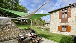 A stone building with wooden shutters, a picnic table set up with plates and glasses, and a green canopy.