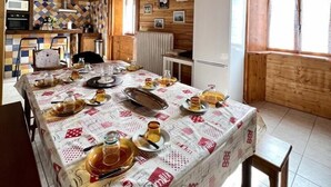 A wooden interior with a dining table set for a meal, a kitchen area, and a refrigerator.