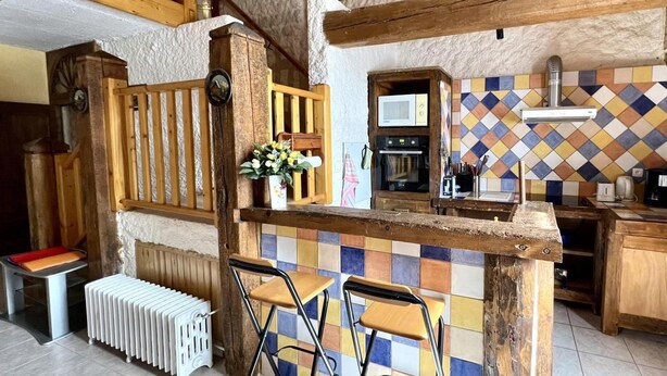 A rustic kitchen with a wooden island, bar stools, a radiator, and a tiled backsplash.