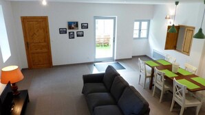A living room with a sofa, a dining table with chairs, a wooden door, and a window. - Alquiere - PUILAURENS (PUILAURENS)