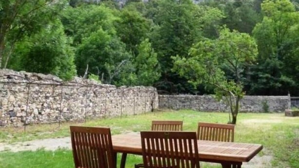 An outdoor dining area with a wooden table and chairs, surrounded by a stone wall and lush greenery, with a mountainous backdrop. - Alquiere - PUILAURENS (PUILAURENS)