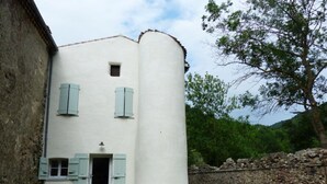 A white building with blue shutters, a stone wall, and a grassy area with a wooden table and chairs. - Alquiere - PUILAURENS (PUILAURENS)