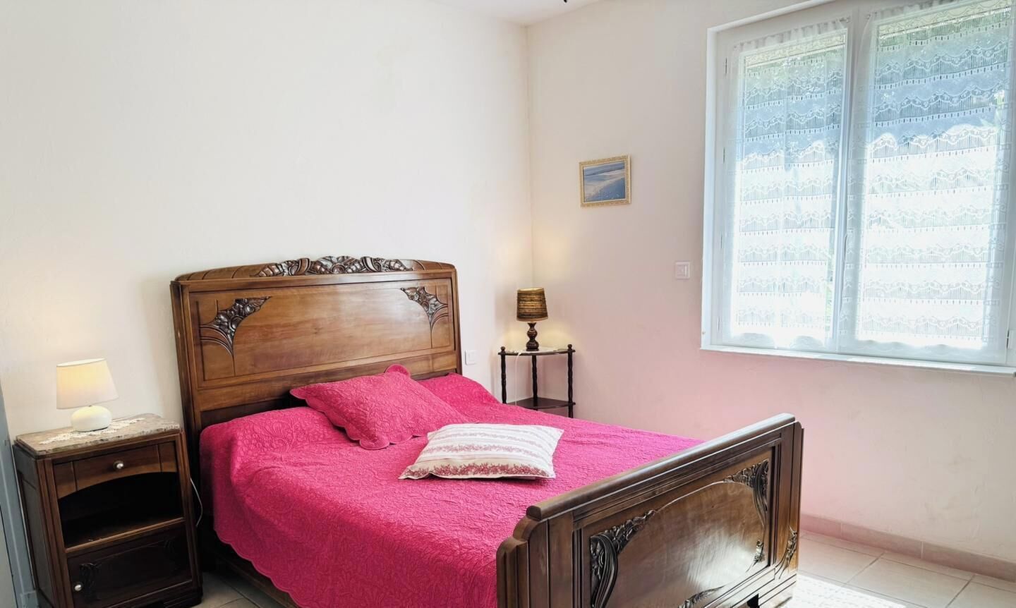 Une chambre à coucher avec un lit en bois, une table de chevet, une lampe et une fenêtre ornée de rideaux en dentelle.