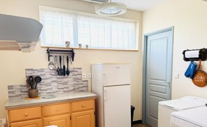 Une cuisine compacte équipée d’un réfrigérateur, d’un lave-linge et d’une fenêtre avec des stores.