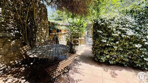 An outdoor patio with a wooden table and benches, surrounded by lush greenery and stone walls. - Le Vigneron - SAINT JEAN DE BARROU (SAINT JEAN DE BARROU)