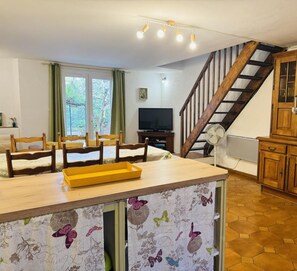 Un salon chaleureux avec un escalier en bois, un coin repas et une cuisine dotée de meubles en bois.