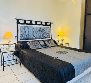 Une chambre à coucher bien rangée, avec un grand lit, deux tables de chevet dotées de lampes et une porte sur le côté droit.