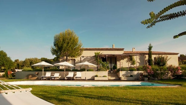 Una casa moderna con piscina, sillas de descanso y sombrillas.
