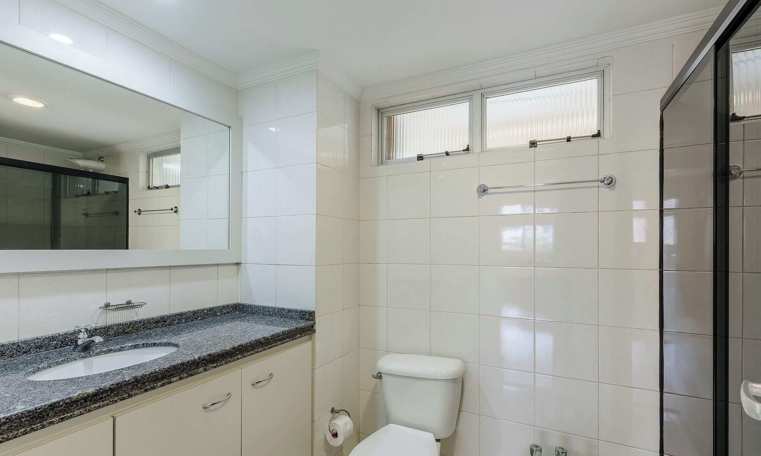 A bathroom with a white toilet, a sink with a granite countertop, and a mirror above the sink.