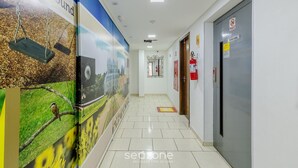 A hallway with a tiled floor, a fire extinguisher, a door labeled "SOCIAL," and a poster of a swing set. - Apartments in a Building 270 m From the Curitiba Botanical Garden - Coss (Curitiba)